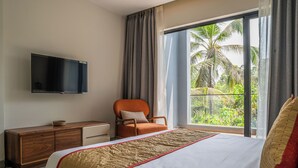 A hotel room with a bed, a TV mounted on the wall, a wooden dresser, and a chair. - Lovely 3-bedroom villa in Saligao with WiFi access (Saligao)