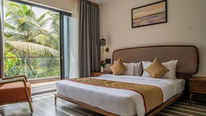 A hotel room with a large bed, a chair, a nightstand, a lamp, and a view of palm trees through a sliding door. - Lovely 3-bedroom villa in Saligao with WiFi access (Saligao)