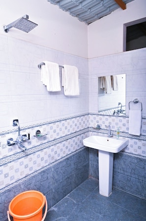 A bathroom with a white sink, a showerhead, a mirror, and a tiled wall with a decorative border. - Hotel The Bagh Village (Sawai Madhopur)