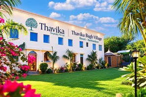 Een wit gebouw met een bord waarop staat 'Thavika Bagh Village Resort - Ranthambore'.