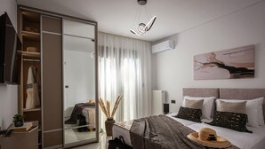 Ein modernes Hotelzimmer mit Schiebetüren zum Kleiderschrank, einem Bett mit vielen Kissen, einem großen Fenster mit durchsichtigen Vorhängen und einer Deckenleuchte.