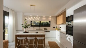 Eine moderne Küche mit einer zentralen Kochinsel, Barhocker, einem eingebauten Backofen und einem Edelstahl-Kühlschrank.