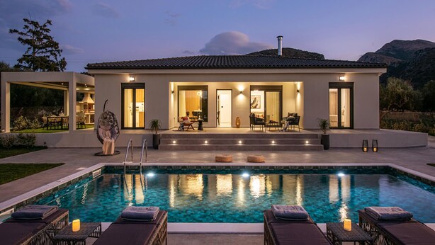Ein modernes Haus mit Schwimmbad, Sitzgelegenheiten im Freien und einem gut beleuchteten Eingang.