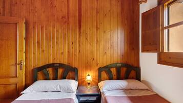 Ein Zimmer mit zwei Holzbettgestellen, einem Nachttisch mit Lampe, Holzwänden und einem Fenster.