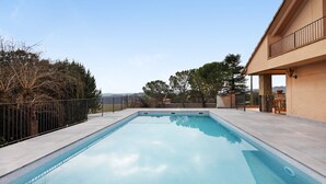 Une piscine rectangulaire à l’eau d’un bleu limpide, entourée d’une terrasse en béton et d’une clôture en métal.