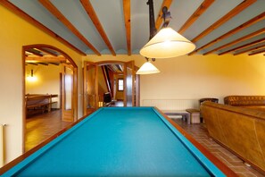 Una mesa de billar en una sala con vigas de madera, un banco y un sofá.