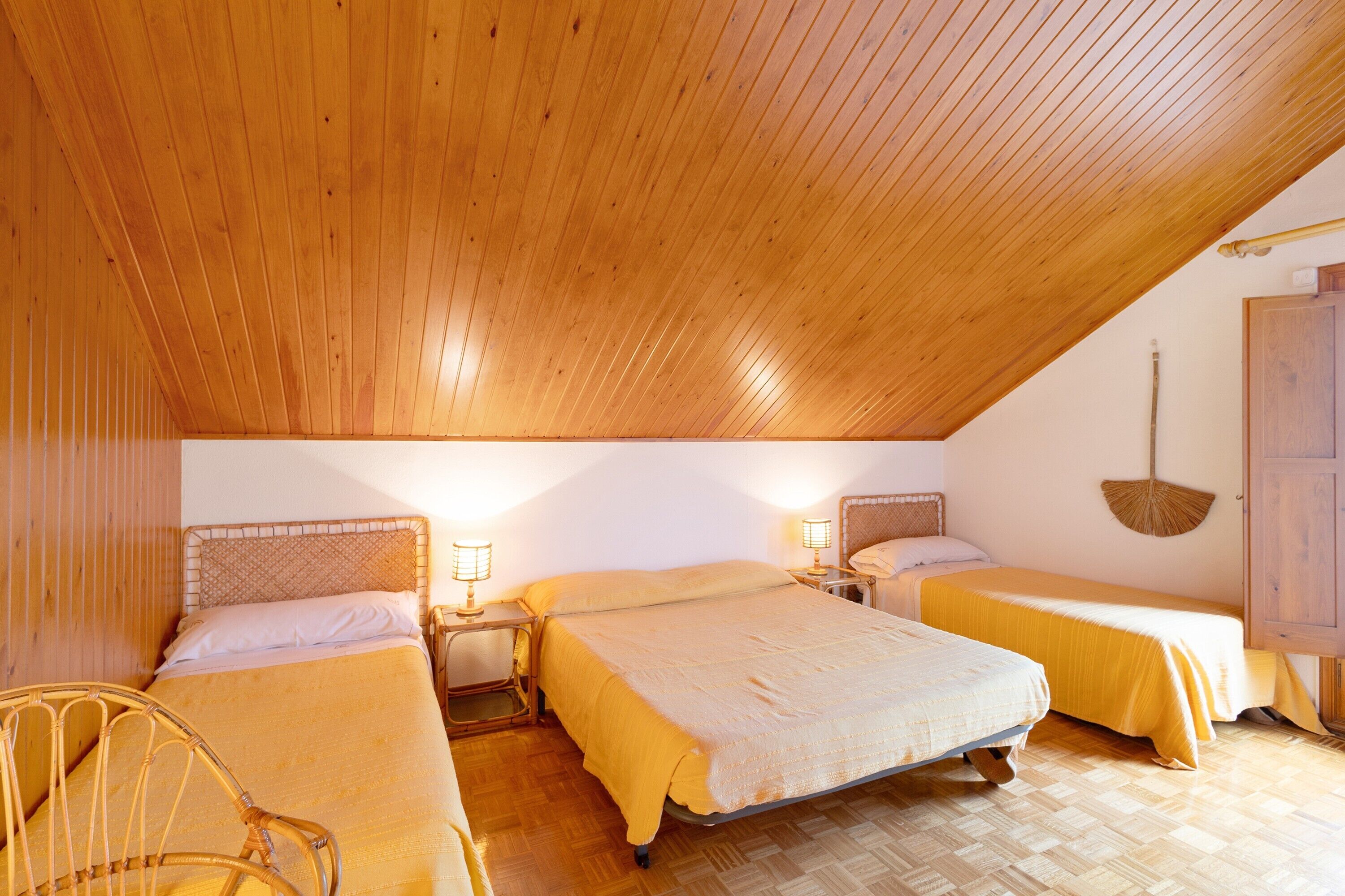 A room with two beds, wooden flooring, and a sloped ceiling.