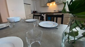 Et spisebord dækket med tallerkener, glas og bestik i et moderne køkken med lyse skabe og en synlig komfur.