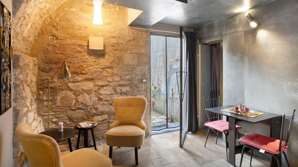 A room with a stone wall, a table with chairs, a floor lamp, and a candle on a side table. - Apartment 'La Cantina' with Sea View, Shared Garden and Wi-Fi (Imperia)
