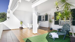 Una terraza en la azotea con césped artificial, una mesa de comedor con sillas, una silla de lounge y plantas en macetas.