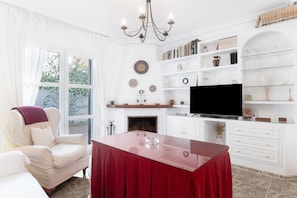 A living room with a TV, bookshelves, a fireplace, and a red table. - Apartment 'Exclusivo Con Vistas' with Private Terrace, Balcony and Wi-Fi (Conil de la Frontera)