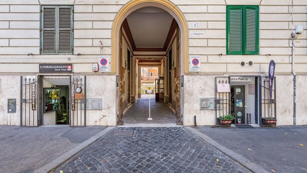 An arched entrance to a building with shops on either side, including a pharmacy and a salon. - Crescenzio St Peter House  (Rome)