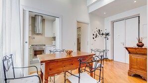 A dining area with a wooden table and metal chairs, a kitchen in the background, and a decorative wall piece. - Crescenzio St Peter House  (Rome)