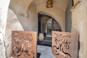 Une porte en arc surmontée d’un décor rustique, un grand pot de fleurs et un portail en métal.