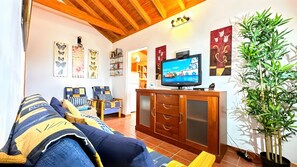 Un salon comprenant un canapé, des fauteuils, un téléviseur, un meuble et des œuvres d’art murales.