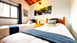 Un lit double avec un couvre-lit bleu, une table de chevet avec une lampe et un tableau représentant une cascade accroché au mur.