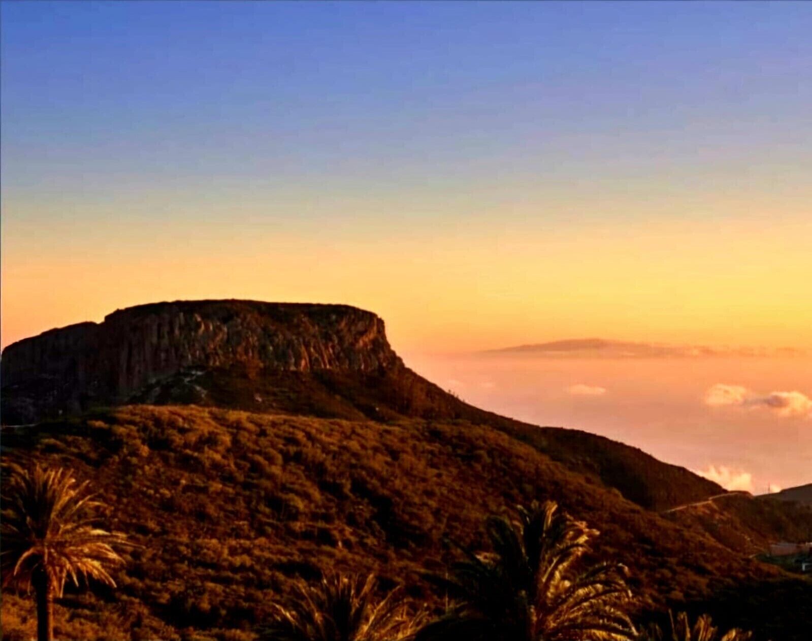 Un paisaje montañoso con un risco destacado y vegetación escasa.