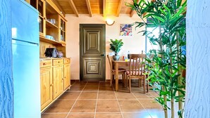 Une cuisine avec des meubles de rangement en bois, un réfrigérateur, une table à manger avec des chaises et une plante en pot.