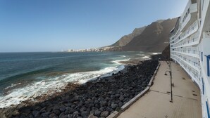 Une vue sur la côte, avec un rivage rocheux, une promenade et un bâtiment doté de balcons donnant sur la mer.