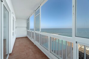 A balcony with a view of the sea, white walls, and a tiled floor.