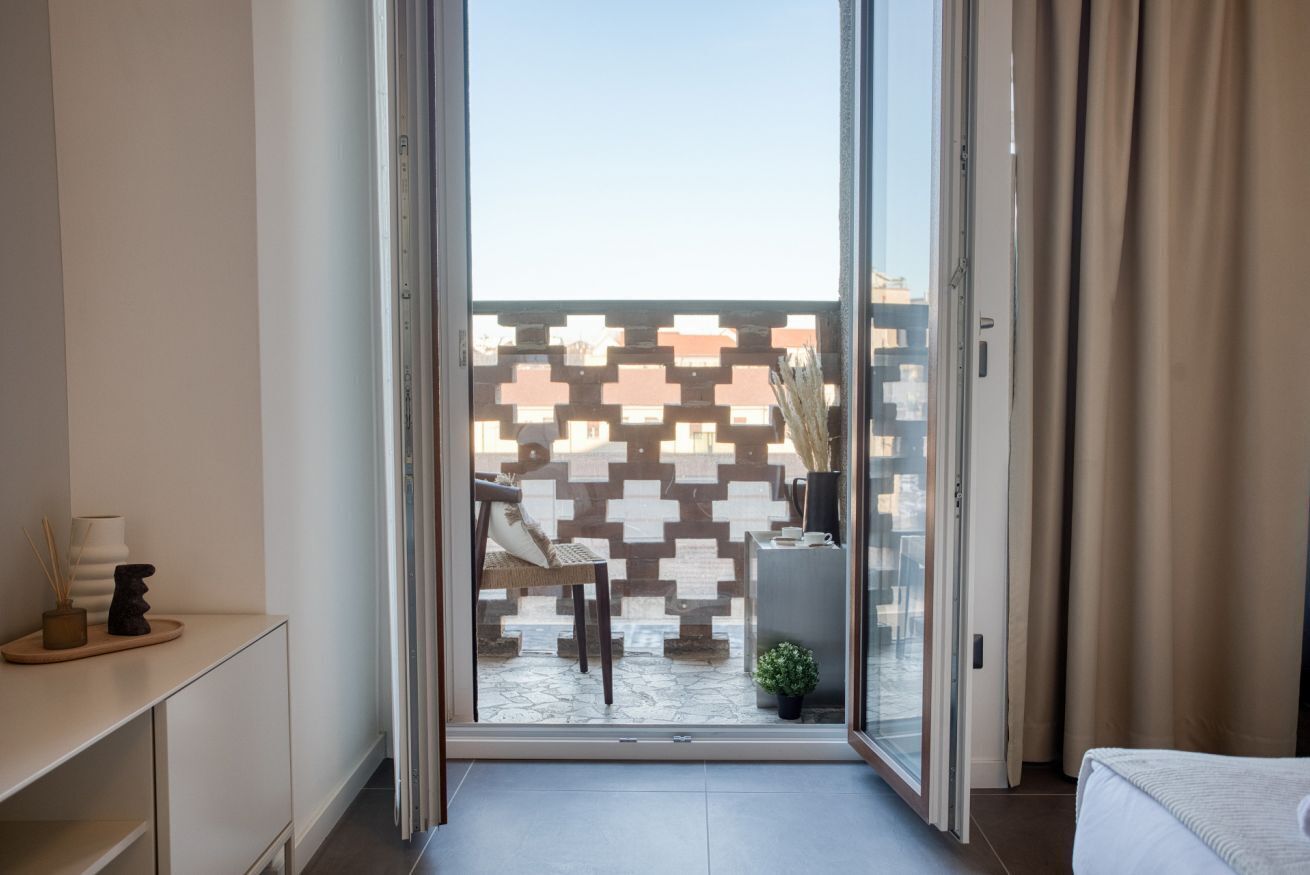 Una camera d'albergo moderna con una porta scorrevole in vetro che dà su uno spazio esterno con un muro decorato e un piccolo giardino.