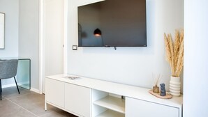 Ein modernes Wohnzimmer mit einem an der Wand befestigten Flachbildfernseher, einem weißen Konsolentisch mit Dekoration und einem Glastisch.