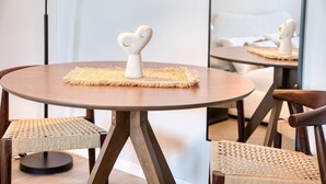 Ein runder Holztisch mit einer gewebten Tischmatte und einem herzförmigen Gegenstand darauf. Zwei Korbstühle stehen um den Tisch herum.