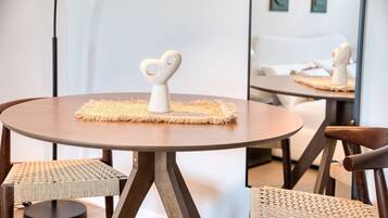 Un tavolo rotondo in legno con un sottotavolo intrecciato e un oggetto a forma di cuore sopra. Due sedie in vimini sono disposte intorno al tavolo.