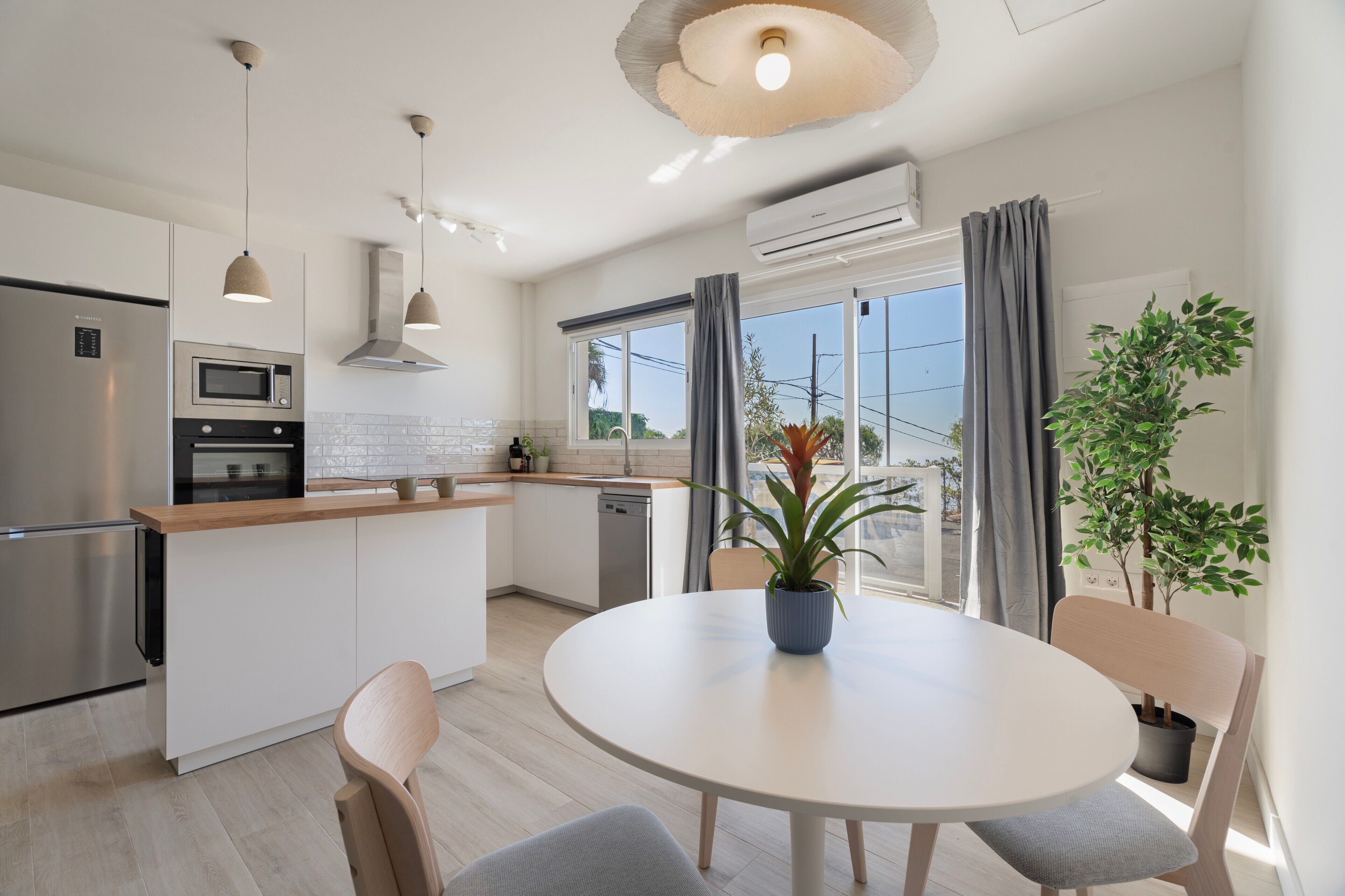 A modern kitchen with a central island, a dining table with chairs, and a potted plant.