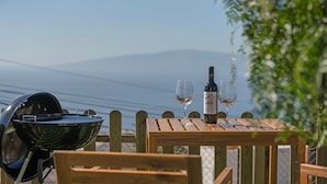Ein Holztisch mit einer Weinflasche und zwei Gläsern, einem Grill und Blick aufs Meer.