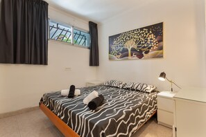 Une chambre à coucher comprenant un lit, une table de chevet, un bureau, une lampe, une fenêtre avec des rideaux et un tableau mural.