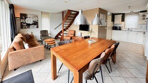 A modern living space with a wooden dining table, cushioned seating, a staircase, and a kitchen area. - 3 bedroom accommodation in Callantsoog (Callantsoog)