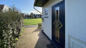 A pathway leading to a house with a dark blue door and a white exterior. - Verhuurburo Callantsoog - De Garnekuul 4 (Callantsoog)