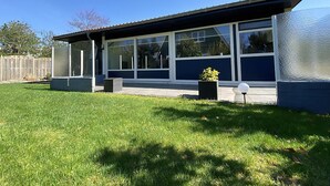 A modern house with large windows, a covered patio, and a well-maintained lawn. - Verhuurburo Callantsoog - De Garnekuul 4 (Callantsoog)