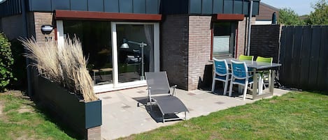 A modern house with a patio, a dining table with chairs, and a large window.
