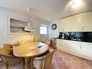 A dining area with a round wooden table, wicker chairs, a white pendant light, and a wall-mounted clock.