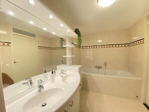 A bathroom with two sinks, a large mirror, and a bathtub.