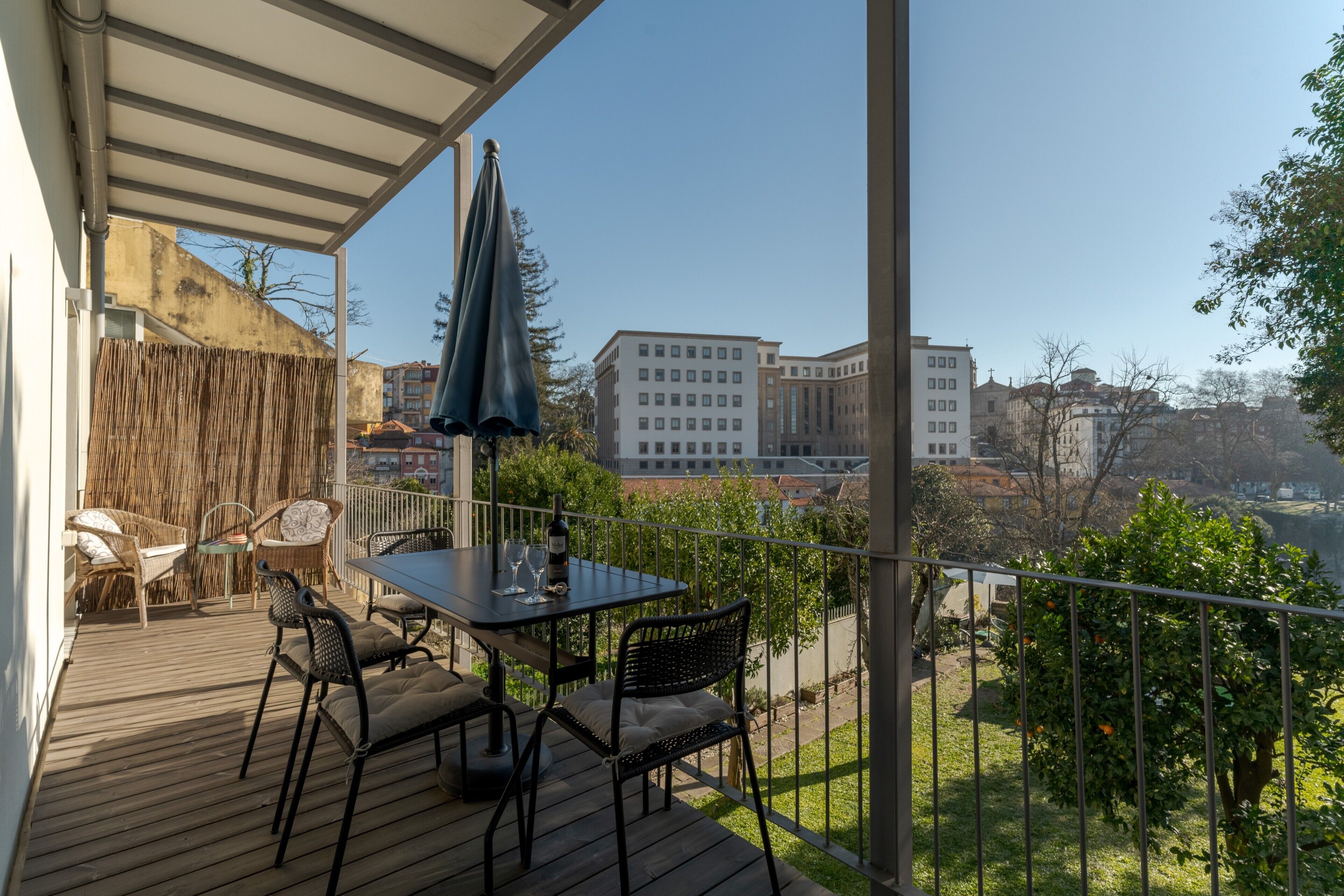 A balcony with a table and chairs, a bottle of wine, and a view of buildings.