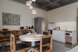 Una cocina moderna con armarios blancos, horno empotrado y comedor con mesa y sillas redondas.