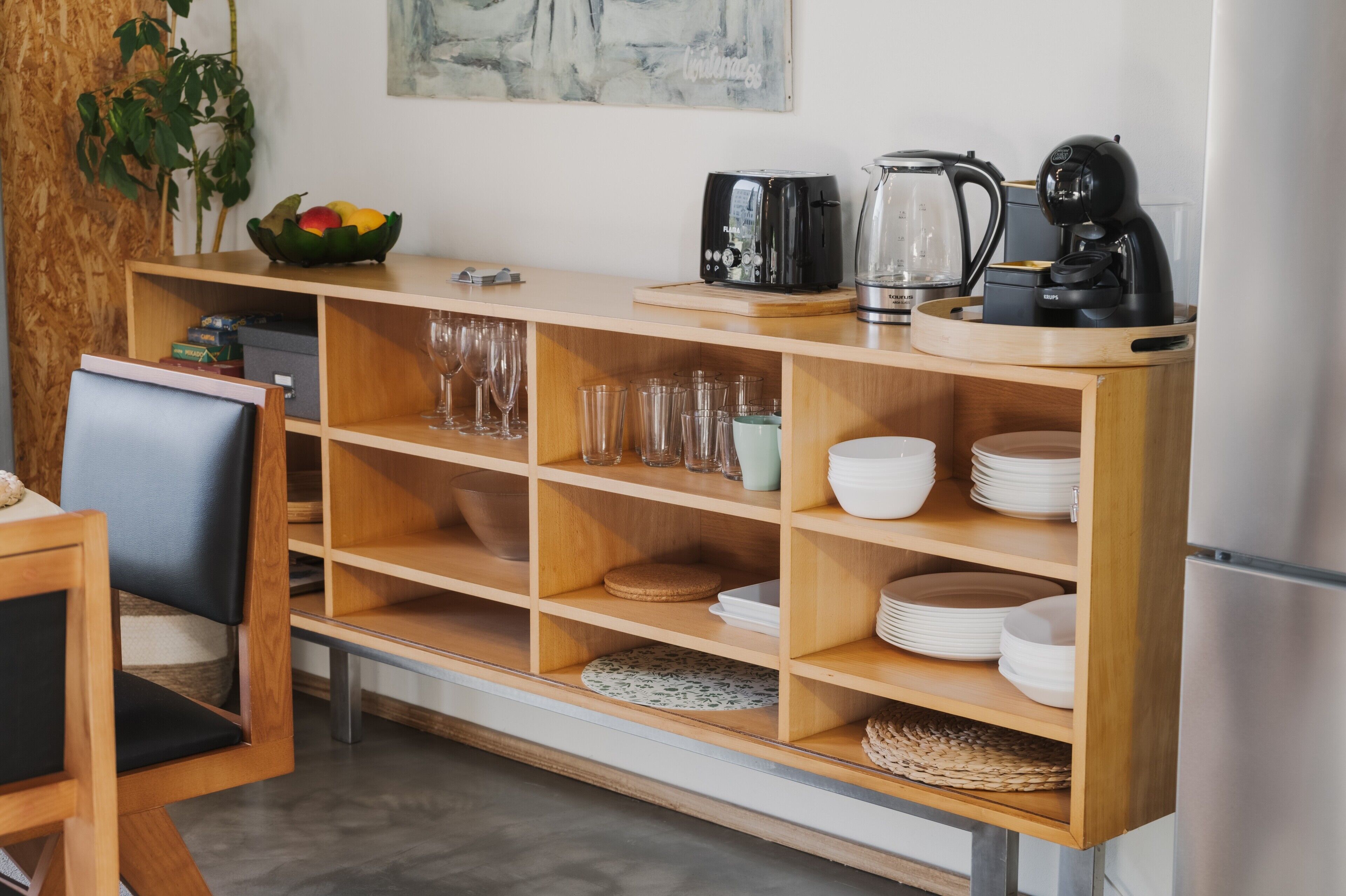 A kitchen with wooden shelves, a coffee maker, a toaster, and a refrigerator.