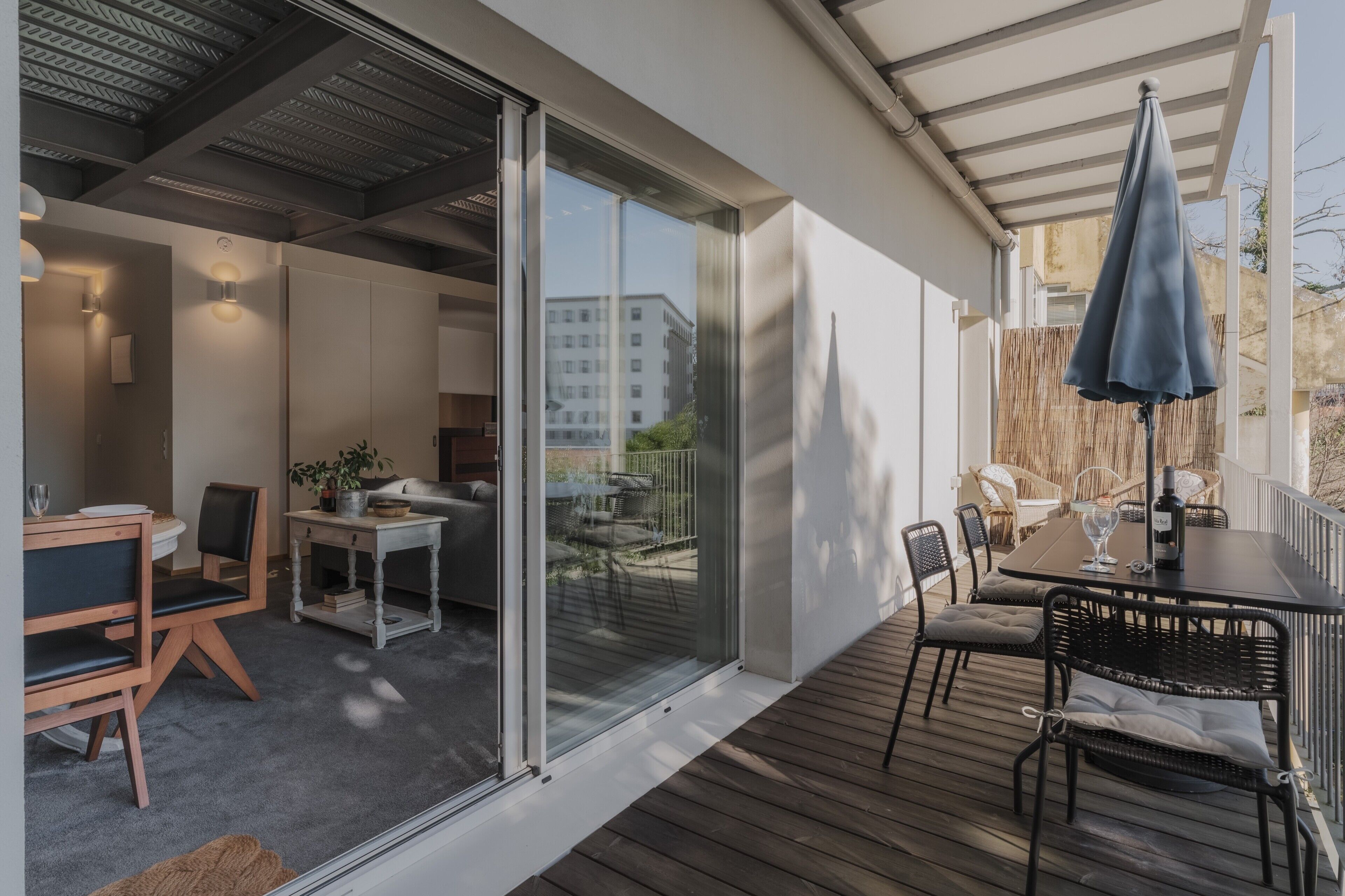 Um pátio moderno ao ar livre com mesa de jantar, cadeiras e um guarda-sol azul.