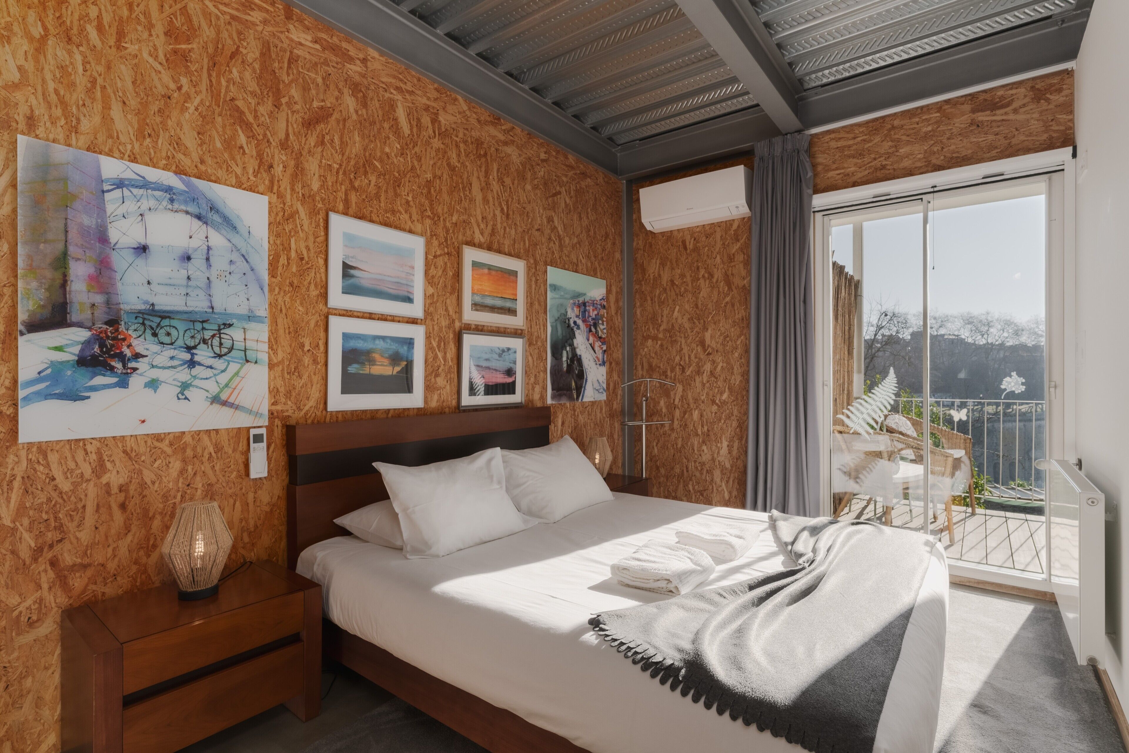 A bedroom with a bed, artwork on the wall, a nightstand, and a balcony with a view.