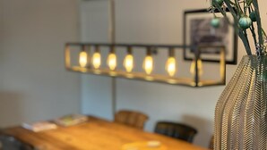 A dining area with a wooden table, chairs, and a hanging light fixture. - Callantsoger Staete A107 (Callantsoog)