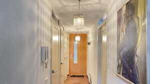 Un couloir orné d’un lustre, avec un grand tableau accroché au mur et une porte sur laquelle est apposée une pancarte.