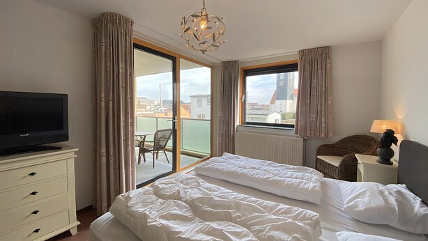 Une chambre d’hôtel équipée d’un lit, d’une télévision, d’un bureau, d’une chaise et d’une fenêtre avec des rideaux.