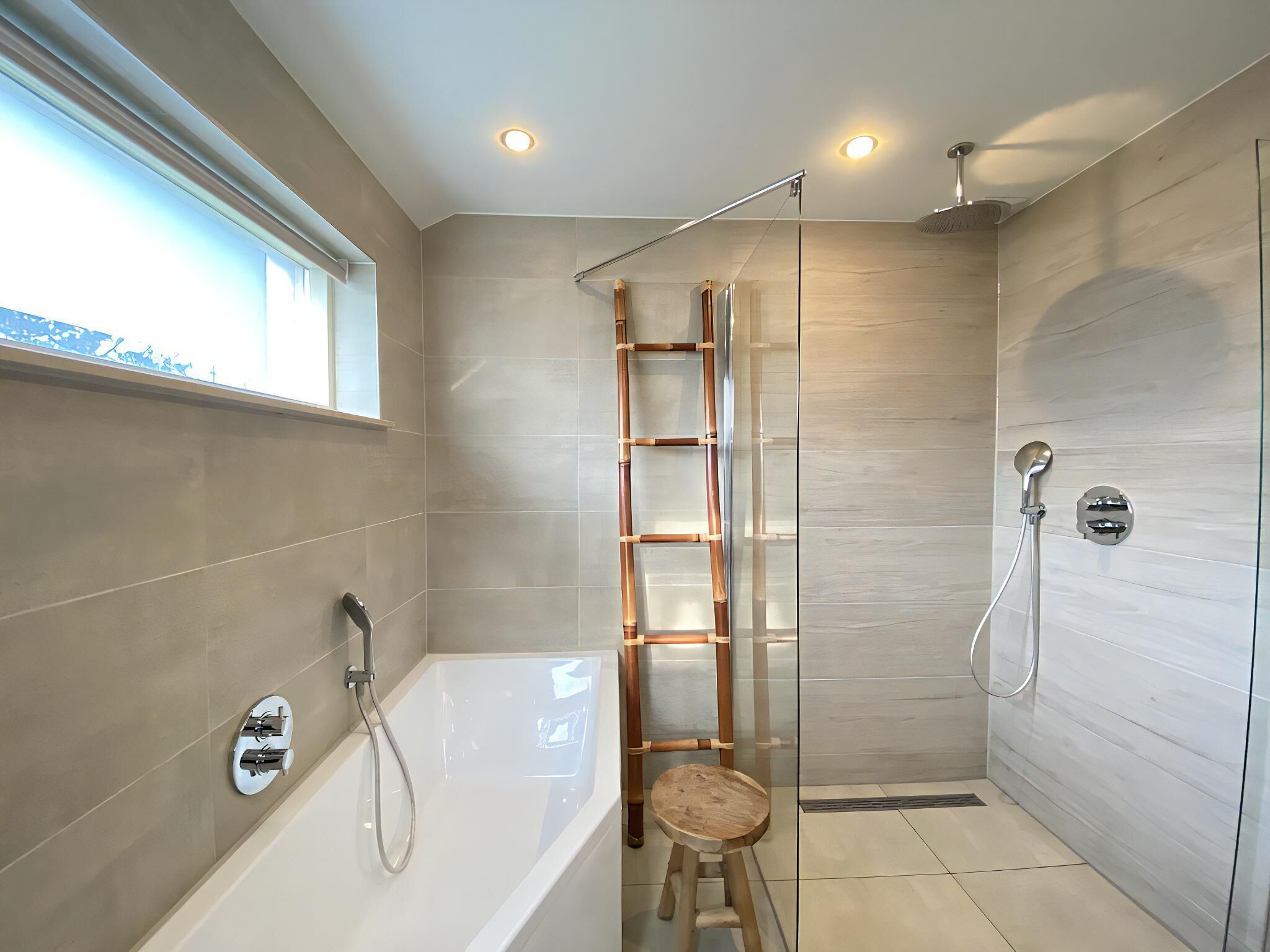 A modern bathroom with a glass shower enclosure, a wooden ladder, a bathtub, and a window providing natural light.