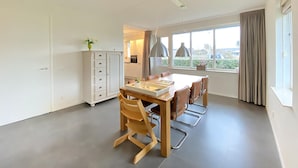A modern kitchen with white cabinets, a dining table with chairs, and a large window with curtains.