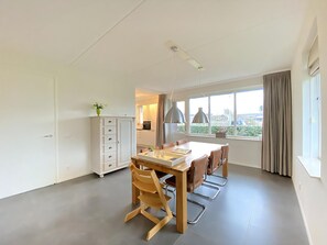 Une cuisine moderne avec des meubles blancs, une table à manger avec des chaises et une grande fenêtre avec des rideaux.