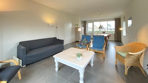 A modern living room with a grey sofa, a white coffee table, blue chairs, and a wicker chair.