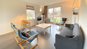 A modern living room with a grey sofa, blue chairs, a white coffee table, and a TV.